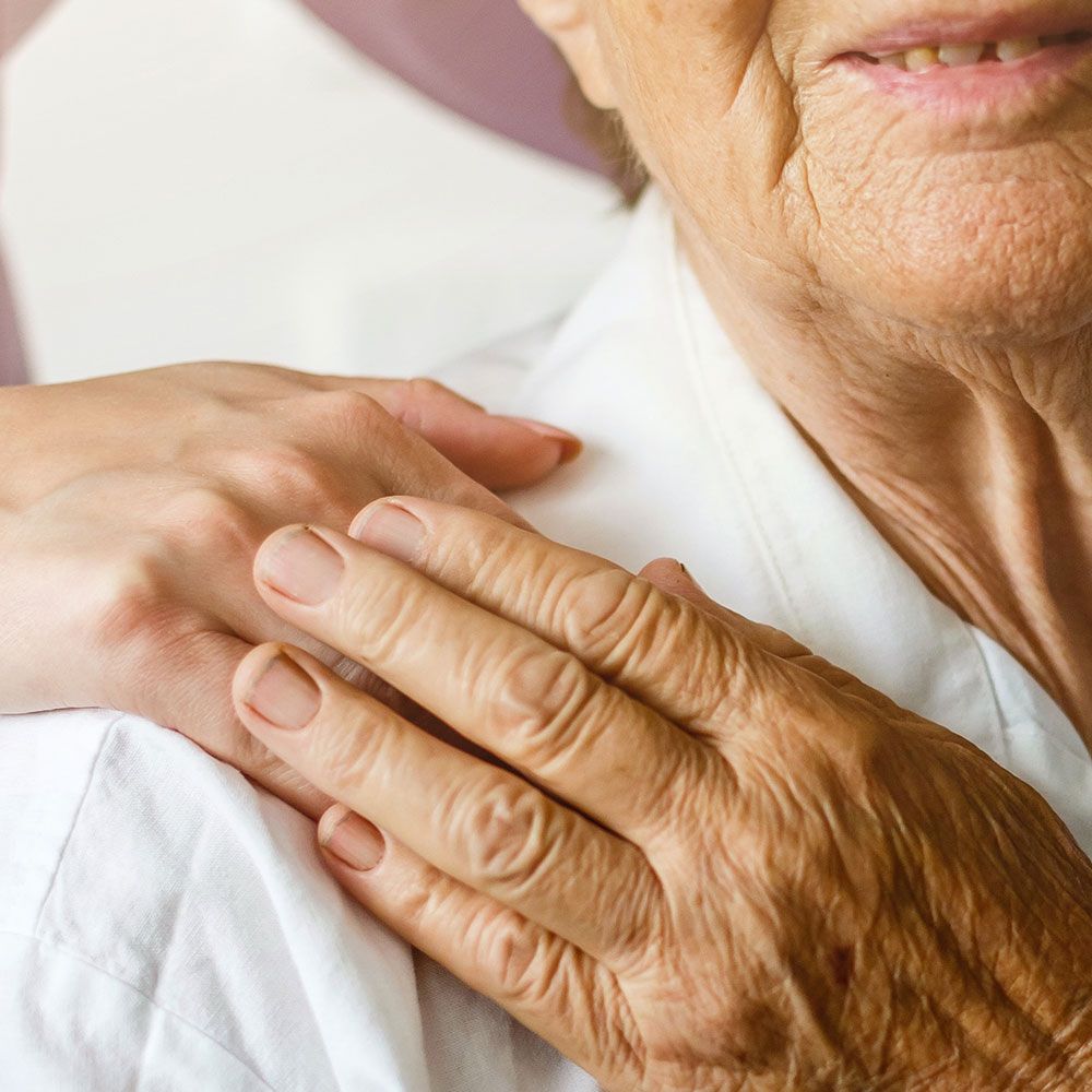 Eine junge Hand ruht auf der Schulter einer älteren Person, unter deren Hand