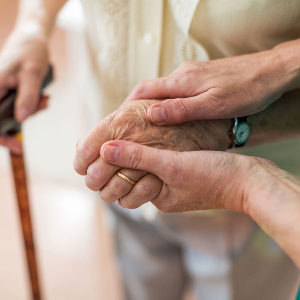 Handhalten einer älteren Person, im Hintergrund ist ein Gehstock zu sehen
